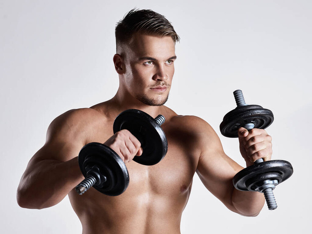 A little progress each day adds up to big results. a sporty young man working out with dumbbells against a grey background - Photo, Image