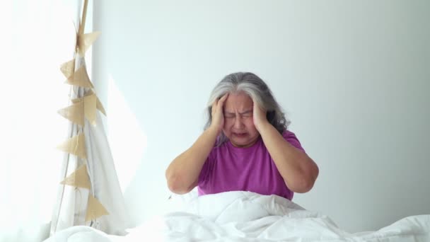 Старша жінка з сірим волоссям в ліжку відчуває себе в депресії або страждає від сильної головного болю мігрені і високого кров'яного тиску, сидячи на самоті. Мігрень Літня Самотня сумна стара жінка тримає голову руками
 - Кадри, відео