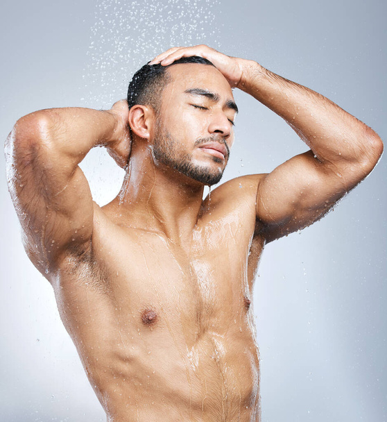 De dag beginnen met een schone noot. Studio shot van een knappe jonge man het nemen van een douche tegen een grijze achtergrond - Foto, afbeelding