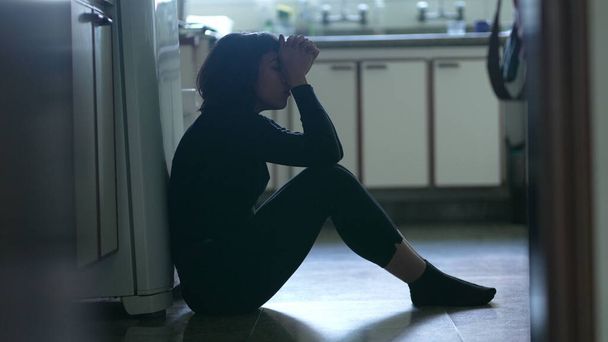 Depressed young woman sitting on kitchen floor feeling desperate in difficult times suffering from mental illness - Photo, Image