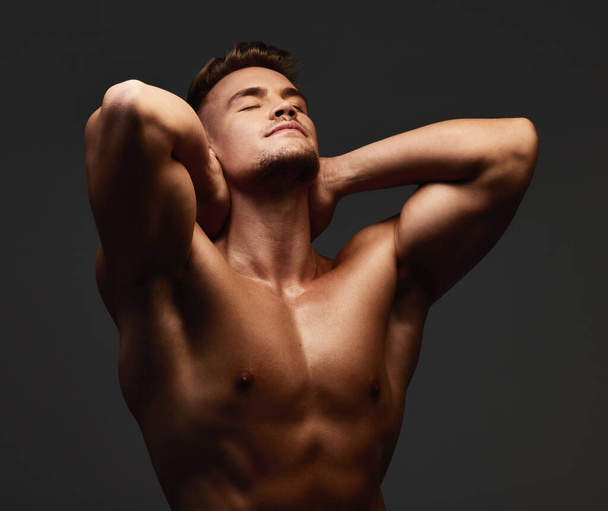 Built like a brick wall. a handsome and athletic young man posing shirtless in studio against a dark background - Zdjęcie, obraz