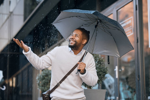 I love the rain. a handsome young businessman walking through the city with an umbrella on a rainy day - Fotoğraf, Görsel
