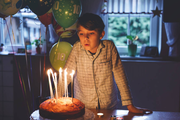 Schattige blonde kleine jongen die zijn verjaardag viert. Kind blaast kaarsen op zelfgebakken taart, binnen. Verjaardagsfeest voor schoolkinderen, familiefeest. - Foto, afbeelding