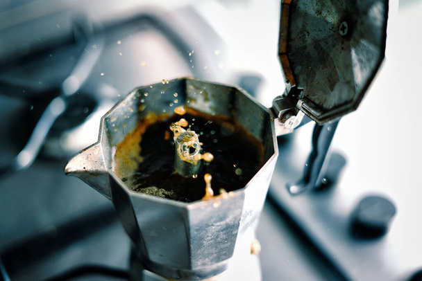 Coffee squirts out of an Italian moka pot with energy. Italian tradition and spitting out espresso. Splashes of black coffee spurting out from the spout and open moka pot stock photo. - Foto, Imagen