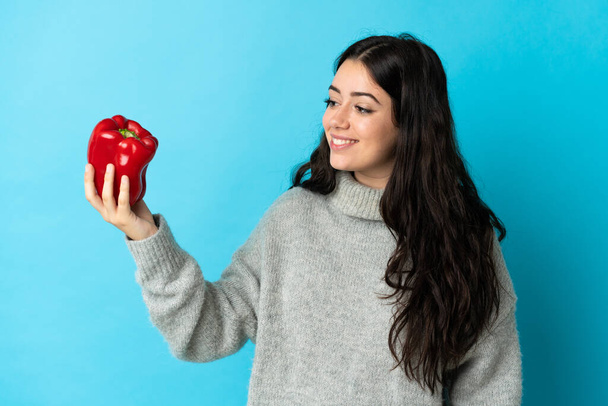Young caucasian woman holding a pepper isolated on blue background with happy expression - Photo, Image