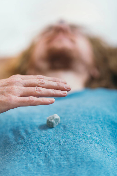 Kristaltherapie. Man liggend op massagetafel, genezing ontvangen met edelstenen geplaatst op lichaam chakra 's - Foto, afbeelding