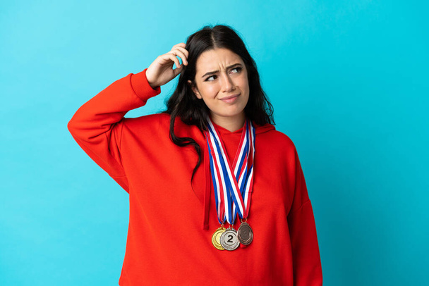 Young woman with medals isolated on white background having doubts and with confuse face expression - Foto, imagen