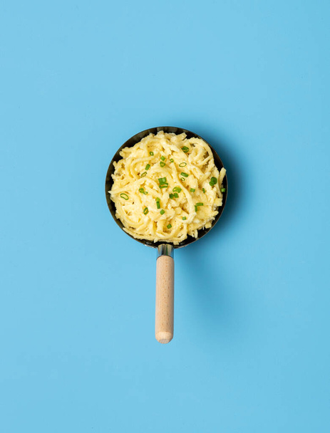 Above view spaetzle in a pan on a blue table. German dish with noodles, cheese and topped with sliced chives. - 写真・画像
