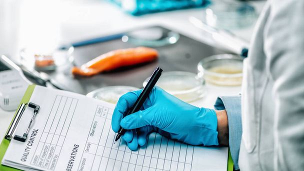 Food safety and quality management. Food safety and quality inspector filling out quality control form in a laboratory, salmon in background - 写真・画像