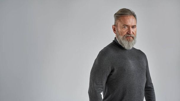 Senior confident caucasian man looking at camera. Stylish bearded pensioner wearing sweater. Concept of modern elderly male lifestyle. Isolated on grey background. Studio shoot. Copy space - Photo, Image