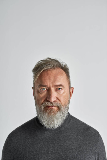 Portrait of senior serious caucasian man looking at camera. Stylish bearded pensioner wearing casual clothes. Modern elderly male lifestyle. Isolated on white background. Studio shoot. Copy space - Фото, изображение