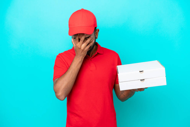 Pizza delivery Brazilian man with work uniform picking up pizza boxes isolated on blue background with tired and sick expression - Foto, Imagen