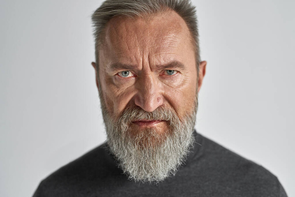 Portrait of ederly serious caucasian man looking at camera. Trendy bearded pensioner wearing sweater. Concept of modern senior male lifestyle. Isolated on white background. Studio shoot - Фото, зображення