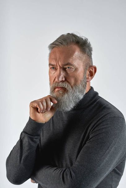 Grey hair thoughtful caucasian man looking away. Fashionable bearded pensioner wearing sweater. Concept of modern elderly male lifestyle. Isolated on white background. Studio shoot. Copy space - Foto, imagen