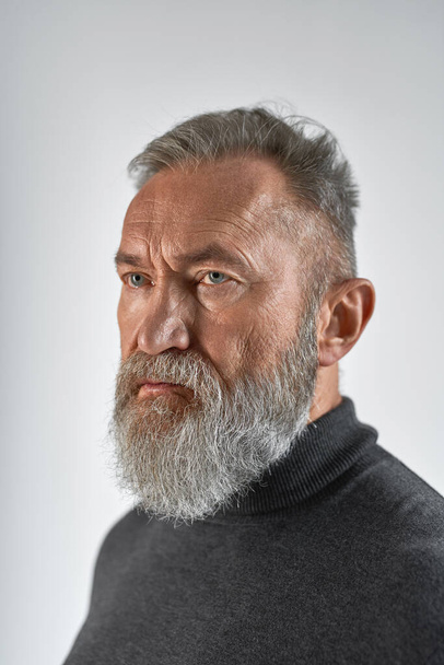 Senior concentrated caucasian man looking away. Stylish bearded pensioner wearing casual clothes. Concept of modern elderly male lifestyle. Isolated on white background. Studio shoot - Foto, afbeelding