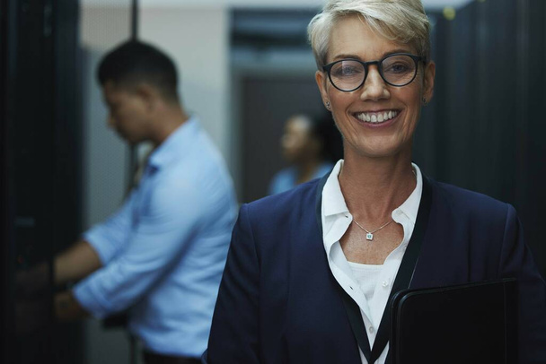 Youll see me when you request their leader. Portrait of a cheerful mature woman working in a server room - Foto, Bild
