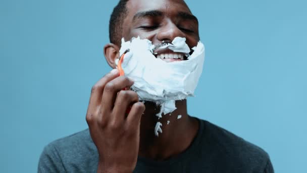 Un uomo si rade la barba con un rasoio e sorride con un primo piano di schiuma da barba. Cura della pelle e concetto di cura del viso. Filmati 4k di alta qualità - Filmati, video