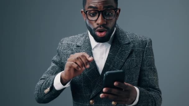 Un uomo afroamericano uomo d'affari con gli occhiali tiene un telefono tra le mani, guarda nel cielo e si rallegra di una proficua transazione commerciale e di reddito. Filmati 4k di alta qualità - Filmati, video