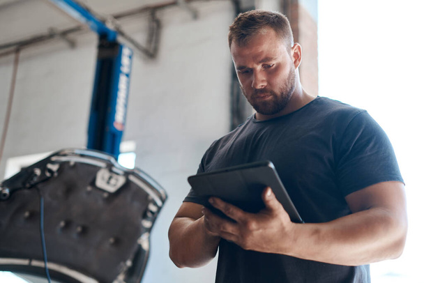 This tool helps us test your car parts without disassembling your vehicle. a mechanic using a digital tablet while working in an auto repair shop - Foto, Imagen