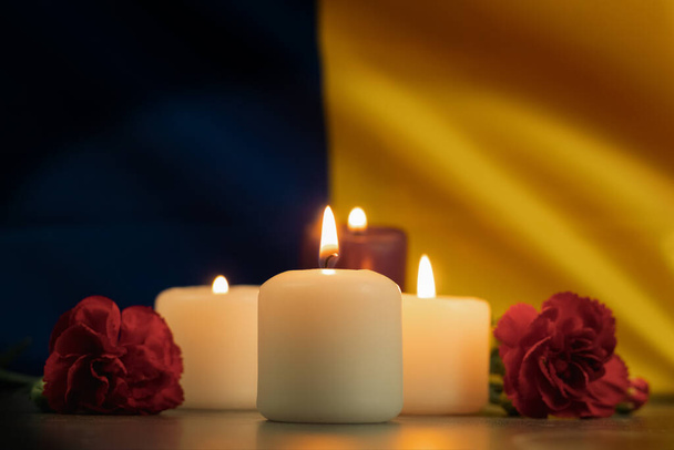 A group of burning candles and flowers on the background of the national flag of Ukraine. Background with copy space. Memory and sorrow with burning candles - Photo, Image