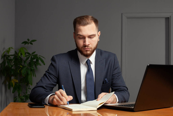 Schöner seriöser Geschäftsmann macht sich Notizen, während er am Laptop arbeitet - Foto, Bild