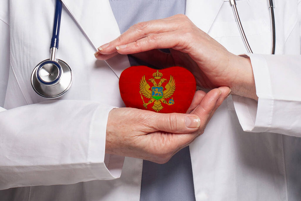 Montenegrin doctor holding heart with flag of Montenegro background. Healthcare, charity, insurance and medicine concept - Photo, Image