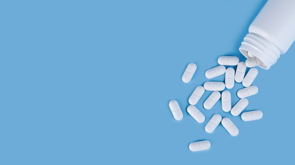 Scattered white pills from the white bottle on blue background. Health care and medicine concept. Close-up. Place for text. - Фото, зображення