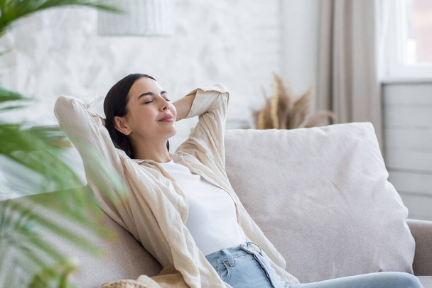Beautiful brunette woman resting with closed eyes during the day, dreaming and dozing at home sitting on the couch - Foto, Imagen