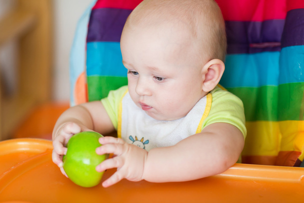 Adorable baby eating apple in high chair - Φωτογραφία, εικόνα