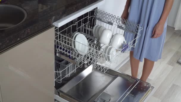Домохозяйка достает чистую посуду с верхней полки посудомоечной машины - Кадры, видео