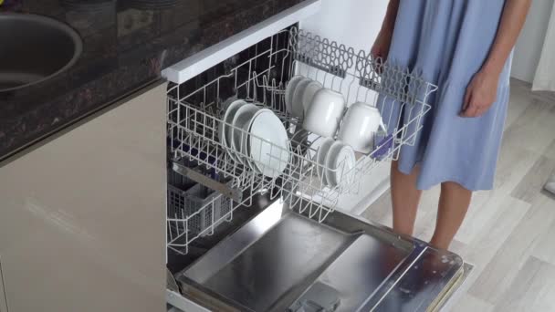 Женские руки вытаскивают чистые тарелки из посудомоечной машины - Кадры, видео