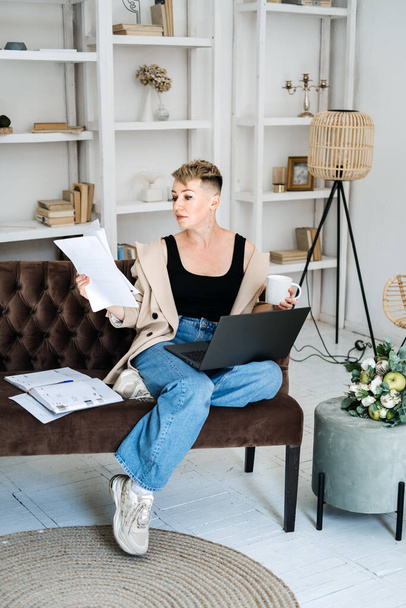 Beautiful hipster woman freelancer copywriter in casual cloth using laptop, writing article and working with papers at home office. Cheerful woman using laptop - Photo, Image