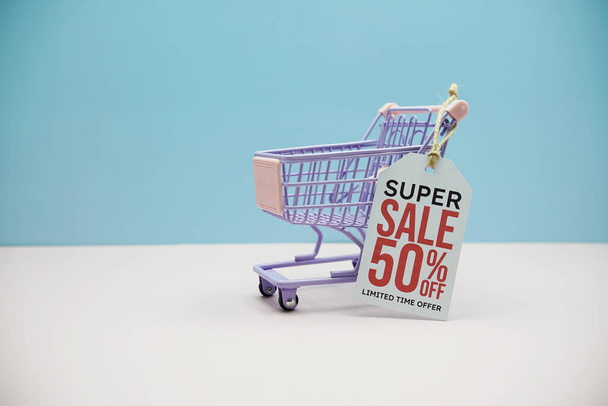 Super Sale 50% off text message and shopping trolley cart on blue and pink background - Fotó, kép