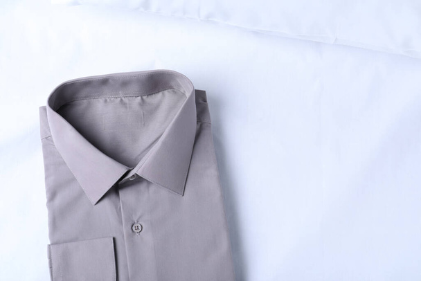 Stylish grey shirt on white fabric, top view with space for text. Dry-cleaning service - Fotografie, Obrázek