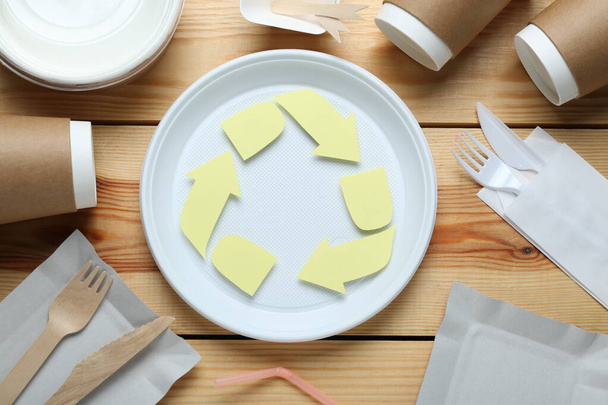 Flat lay composition with disposable dishware and recycling symbol on wooden table - Fotografie, Obrázek