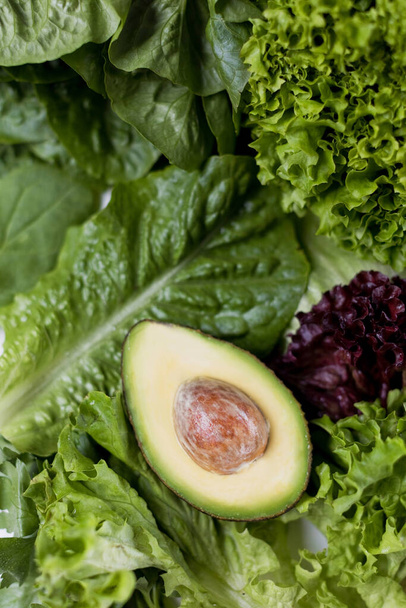 Ripe avocado and mix of green lettuce leaves close up. Healthy eating, vegetarian vegan food concept - Φωτογραφία, εικόνα