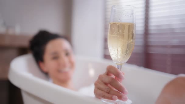 Out of focus young happy relaxed woman lying in foam bath holding glass champagne funny playful lady blowing on foam in bathroom enjoying flavorous alcoholic drink luxurious recreation for weekend - Séquence, vidéo