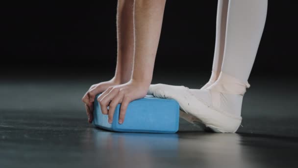 Unrecognizable girl ballerina gymnast dancer teenager bending standing feet in pointe shoes ballet shoes doing stretching using yoga block rectangle blue sports equipment stretch with brick exercise - Filmati, video