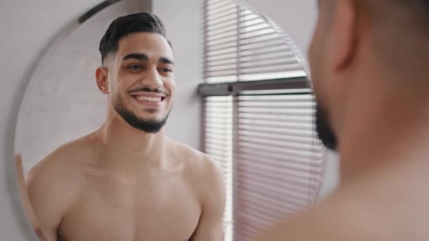 30s Arabian brunette Indian model man with beard looking smiling to himself reflection in mirror in home hotel bath millennial guy face smile toothy in morning in bathroom evening hygienic procedure - Video