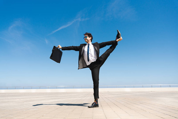 Happy and handsome adult businessman wearing elegant suit doing acrobatic trick moves in the city, alternative concept for business advertisement with energetic and creative people - Foto, Imagen