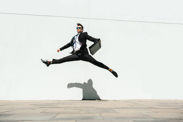 Happy and handsome adult businessman wearing elegant suit doing acrobatic trick moves in the city, alternative concept for business advertisement with energetic and creative people - Photo, image