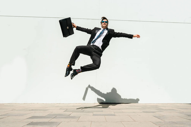 Happy and handsome adult businessman wearing elegant suit doing acrobatic trick moves in the city, alternative concept for business advertisement with energetic and creative people - Фото, изображение