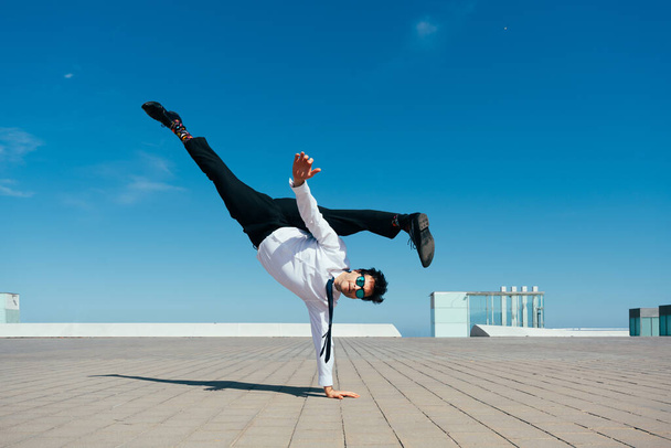 Happy and handsome adult businessman wearing elegant suit doing acrobatic trick moves in the city, alternative concept for business advertisement with energetic and creative people - Foto, Imagem