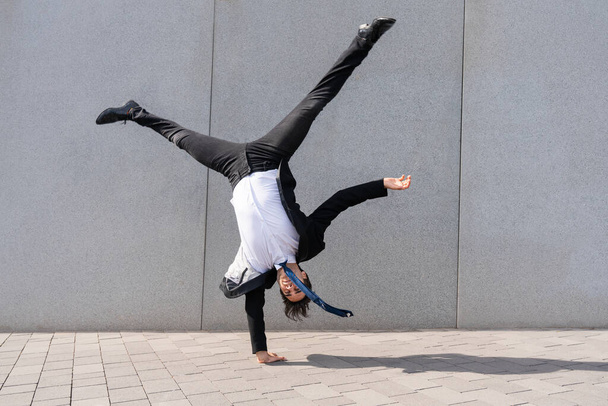 Happy and handsome adult businessman wearing elegant suit doing acrobatic trick moves in the city, alternative concept for business advertisement with energetic and creative people - Фото, зображення