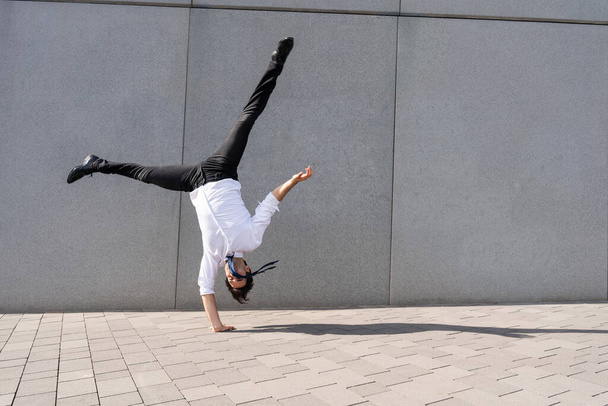 Happy and handsome adult businessman wearing elegant suit doing acrobatic trick moves in the city, alternative concept for business advertisement with energetic and creative people - Foto, Bild