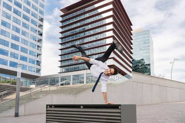 Happy and handsome adult businessman wearing elegant suit doing acrobatic trick moves in the city, alternative concept for business advertisement with energetic and creative people - Fotoğraf, Görsel