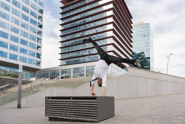 Vrolijke en knappe volwassen zakenman draagt elegant pak doet acrobatische truc beweegt in de stad, alternatief concept voor zakelijke reclame met energieke en creatieve mensen - Foto, afbeelding