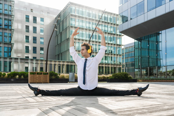 Happy and handsome adult businessman wearing elegant suit doing acrobatic trick moves in the city, alternative concept for business advertisement with energetic and creative people - Zdjęcie, obraz