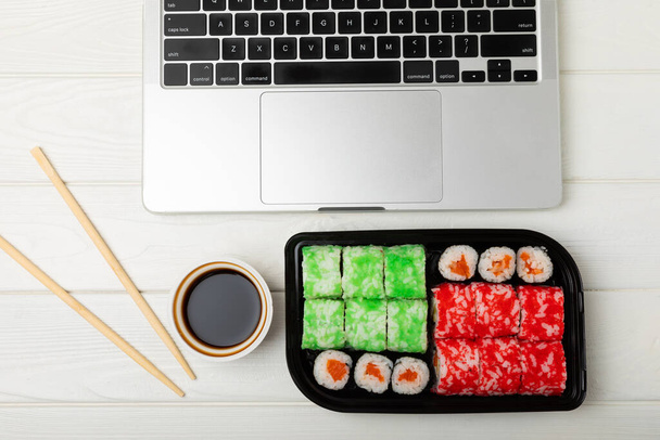 Office work, lunches and home delivery. Seafood sushi set on white table with laptop and blank screen. Food delivery concept.Japanese food.Copy space. Place for text. - Фото, изображение