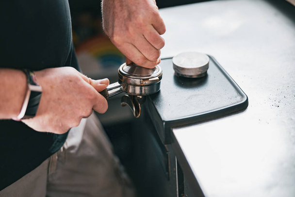Barista holding tamper and press ground coffee in holder to make espresso for client in cafe - Zdjęcie, obraz